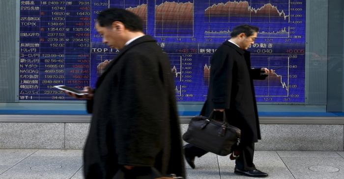 FILE PHOTO: Men walk past an electronic board showing market indices outside a brokerage in