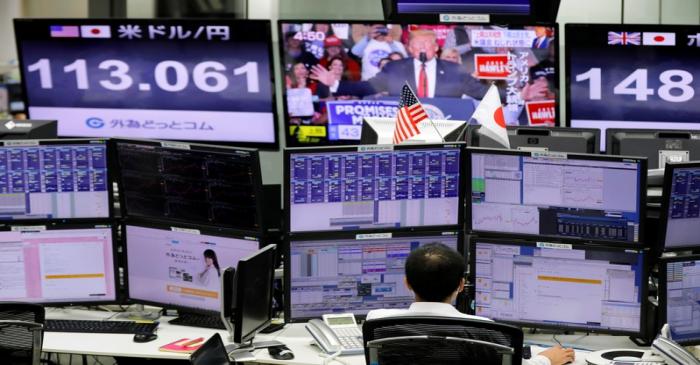 An employee of a foreign exchange trading company works in front of monitors showing TV news on