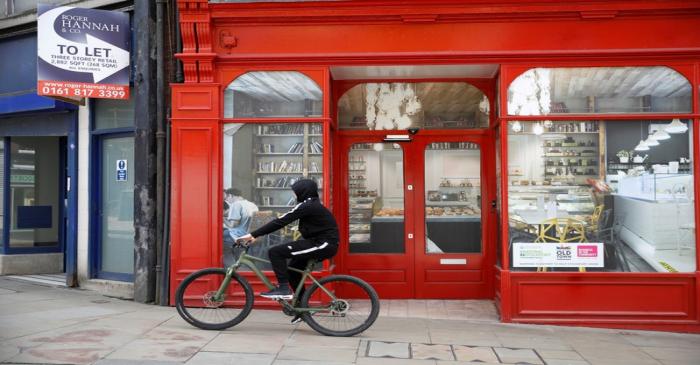 A boy cycles past a closed down retail unit for rent in Stockport, near Manchester