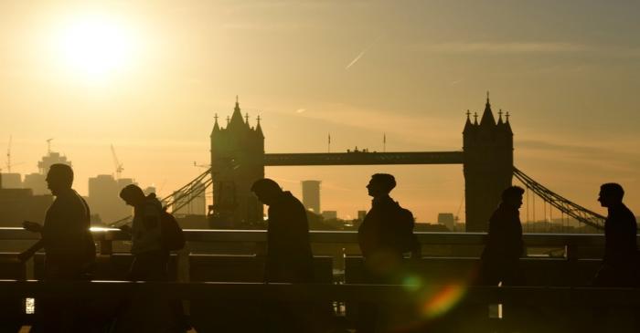 Workers are seen crossing London Bridge with Tower Bridge seen behind during the morning rush