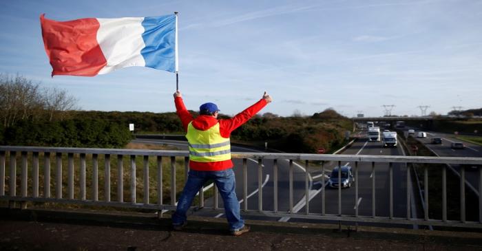 A man wearing a yellow vest and holding a French flag stands on a bridge near the Nantes