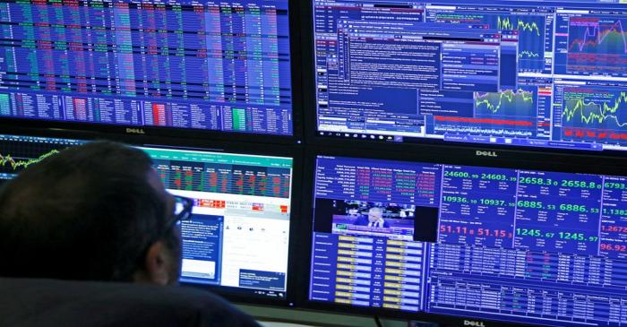 Traders work at their desks whilst screens show market data at CMC Markets in London