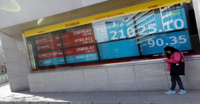 A woman stands in front of a screen displaying Japan's Nikkei share average, U.S. and other