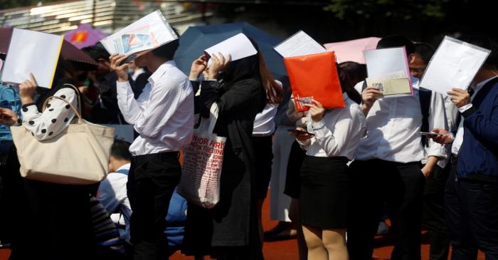 Students shield themselves from the sun as they line up at a job fair at a university in