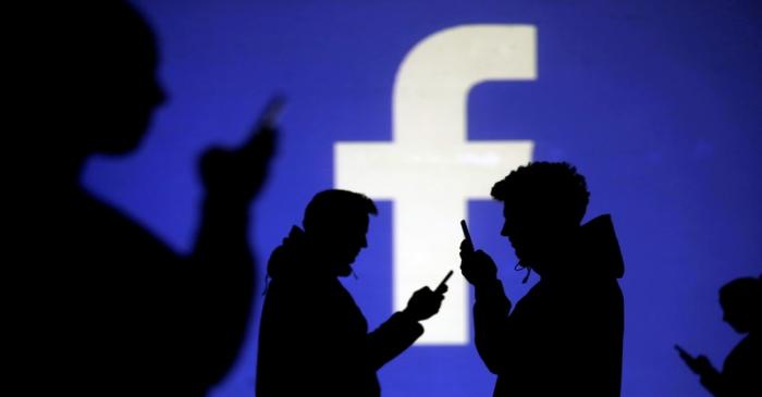 FILE PHOTO: Silhouettes of mobile users are seen next to a screen projection of Facebook logo