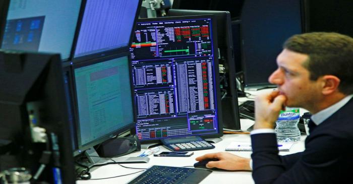 Traders work at their desks whilst screens show market data at CMC Markets in London