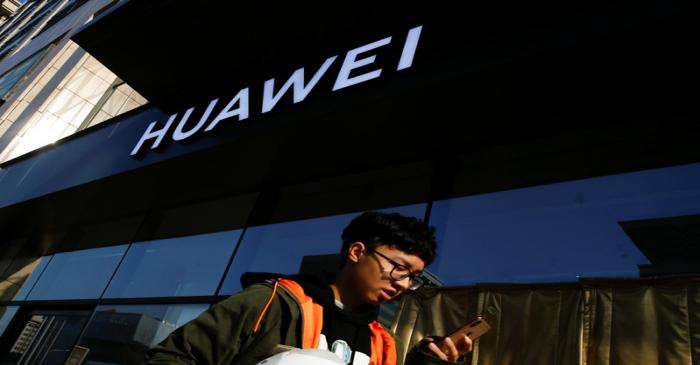 A man uses his phone as he walks past a Huawei shop in Beijing