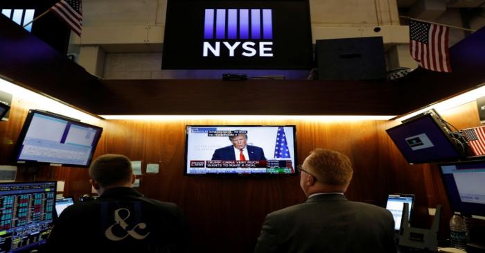 Traders watch monitors displaying a media conference with U.S. President Donald Trump live at