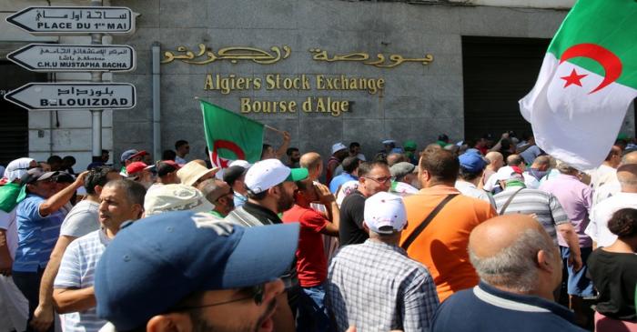 Demonstrators carry flags as they walk past Algiers Stock Exchange during an anti-government