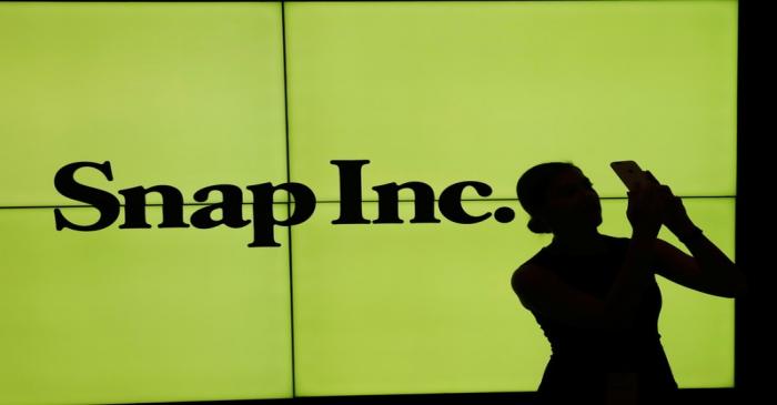 A woman stands in front of the logo of Snap Inc. on the floor of the New York Stock Exchange