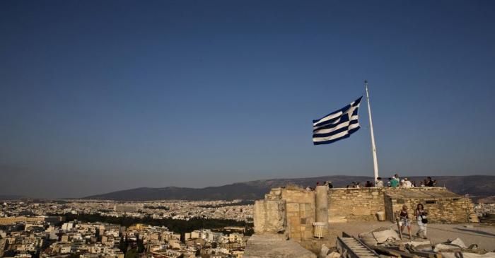 Greek flag flutters in the wind as tourists visit the archaeological site of the Acropolis hill