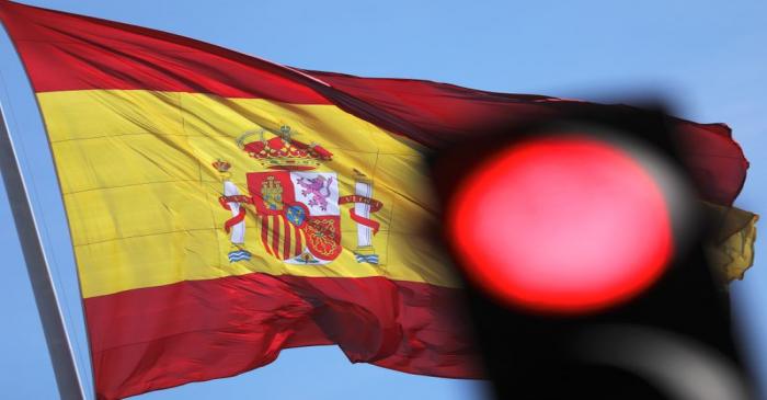 A Spanish flag flutters behind a red traffic light in Madrid