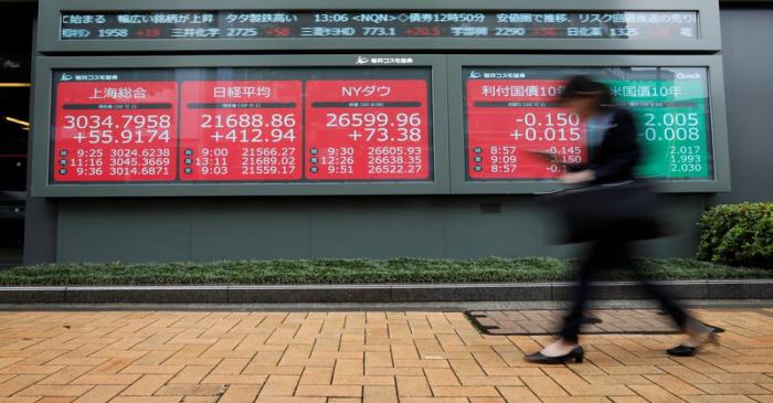 A woman walks past an electric screen showing world markets indices outside a brokerage in