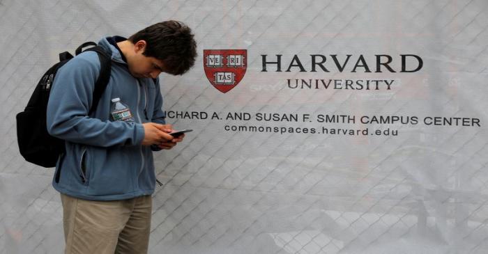 FILE PHOTO: A man looks at his mobile phone beside a sign for Harvard University in Cambridge