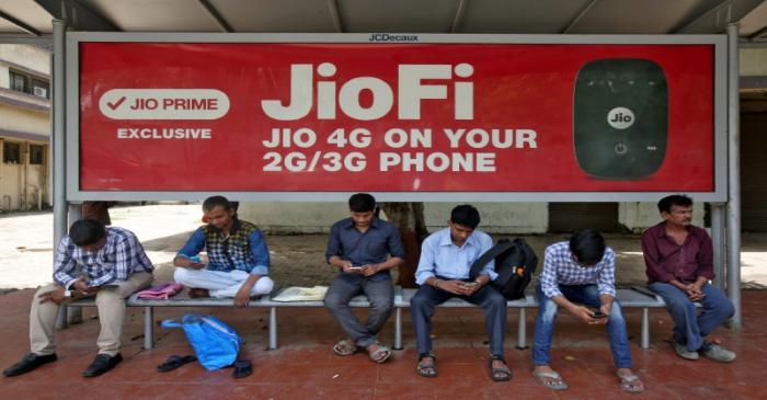 FILE PHOTO: Commuters use their mobile phones as they wait at a bus stop with an advertisement