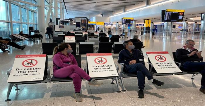 FILE PHOTO: People sit amongst socially-distanced seating signs at Heathrow Airport in London