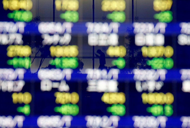 A man in a business building is reflected on an electronic stock quotation board outside a