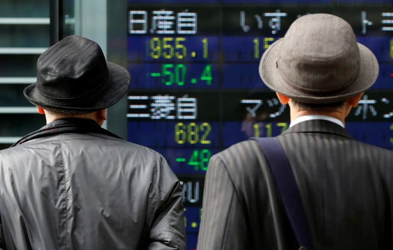 Men look at a stock quotation board showing share prices of Nissan Motor Co and Mitsubishi