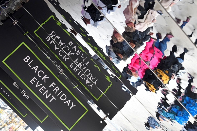 Black Friday signage and shoppers are reflected in puddles on Oxford Street in London