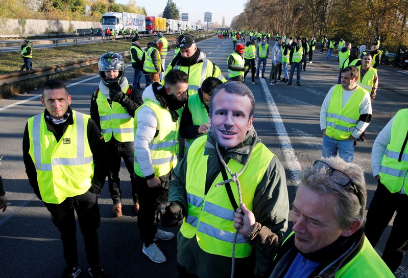 FILE PHOTO: A man wears a mask with the likeness of French president Emmanuel Macron as people