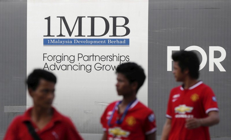 Men walk past a 1Malaysia Development Berhad (1MDB) billboard at the fund's flagship Tun Razak