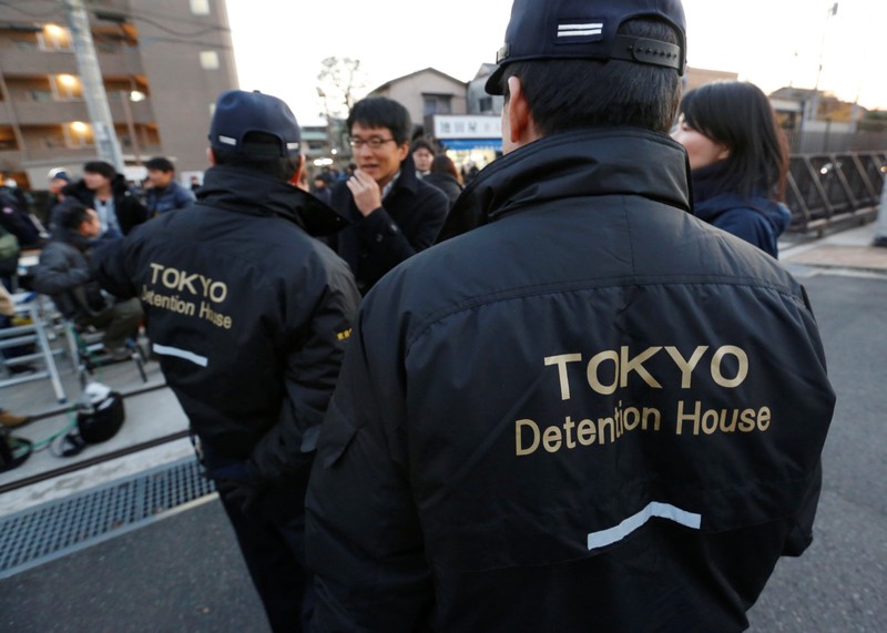 Security officers talk with media members at the gate of Tokyo Detention Center, where Nissan's