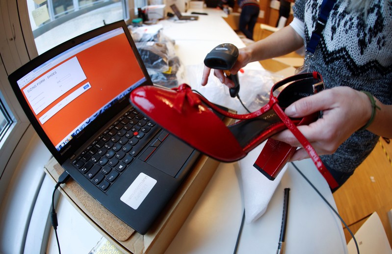 A fitting model enters data in a laptop after she checks out sizes for a shoe which goes on