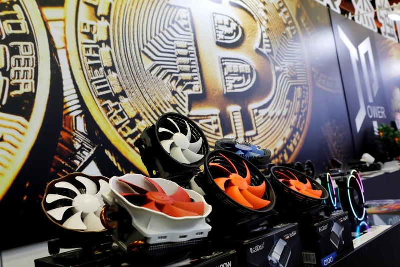 Cryptocurrency mining computer fans are seen in front of bitcoin logo during the annual