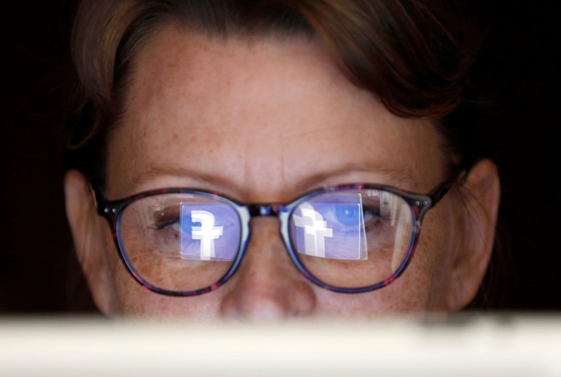 The Facebook logo is reflected on a woman's glasses in this photo illustration