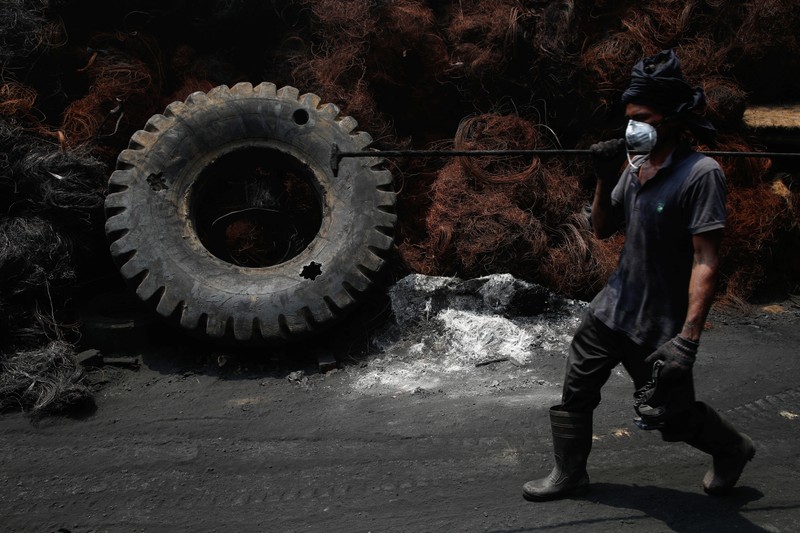 A worker passes steel wires and a tyre at a tyre pyrolysis plant in Kulai