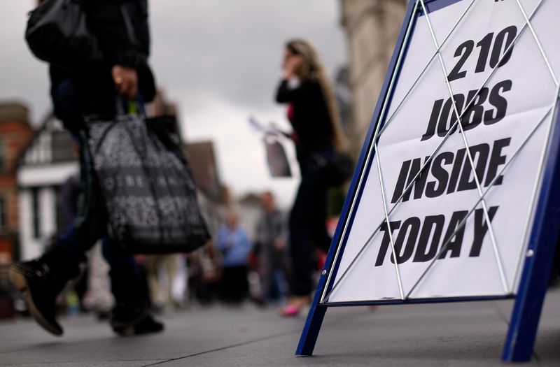 Shoppers walk past a newspaper advertising board promoting its job supplement in Leicester,