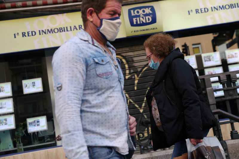 FILE PHOTO: People wearing protective face masks walk past a real estate agency during the