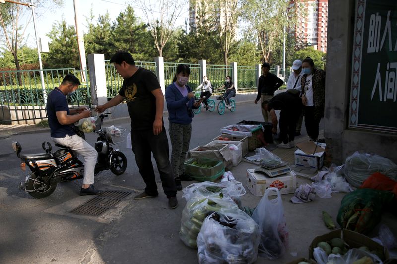 Street vendors sell vegetables and fruits at a stall by a river near a residential area in